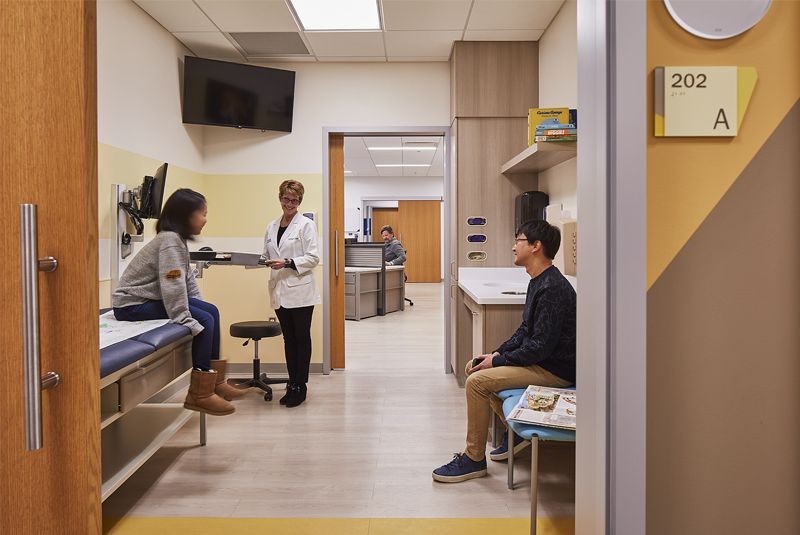 Exam room accessible by large sliding doors with a child sitting in the patient chair and a doctor smiling as talking to the child.