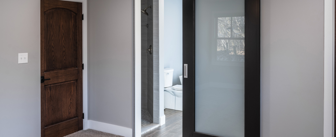 Modern residential room featuring a black-framed sliding glass door leading to a bathroom, showcasing space efficiency and contemporary design.