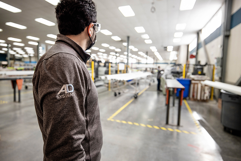 AD Systems employee in branded long-sleeve shirt working in a door manufacturing factory, showcasing the company's production environment.