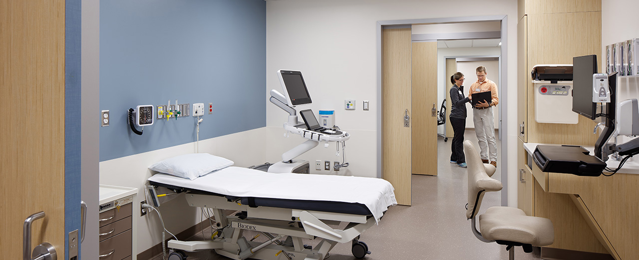 Standard patient exam room with blue wall and a sliding door creating a flexible design between rooms.