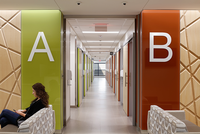 Hallway in healthcare space with sliding doors creating multiple flexible rooms with woman sitting on a couch in the front.