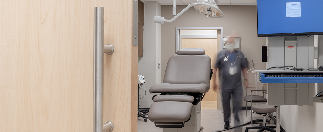 Close up image of sliding exam room door partially open to show a medical professional moving through the exam room.