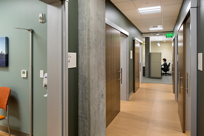 Image of a hallway in a healthcare facility with sliding exam room doors open for use.