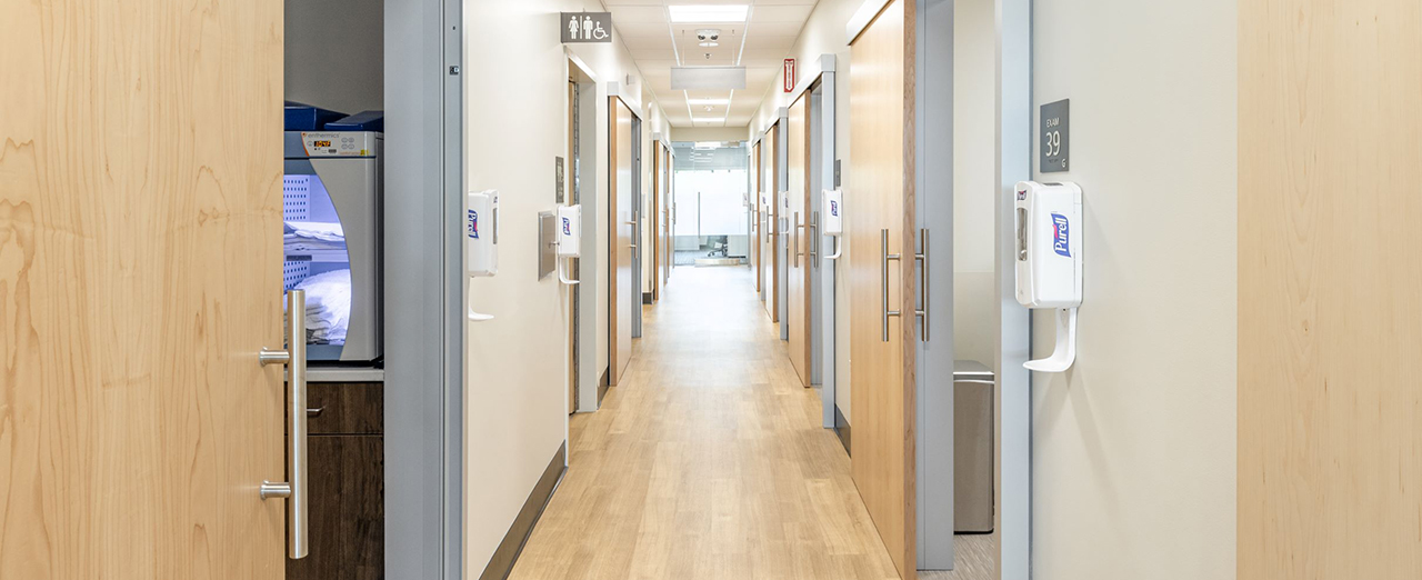 Light wood-toned hallway with sliding doors leading into patient rooms.