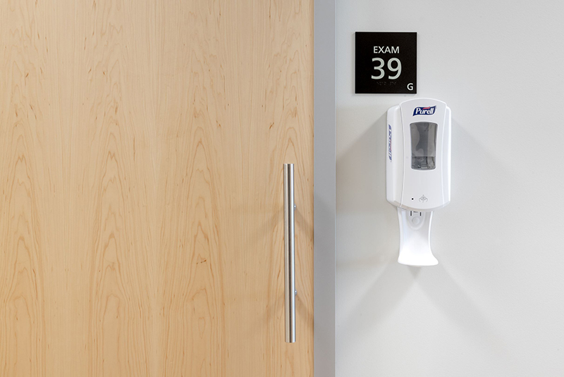 Close-up view of wood exam room sliding door with hand sanitizer outside on the wall. 