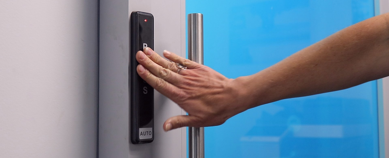 Person pressing an electric door opening presspad for an automatic sliding door.