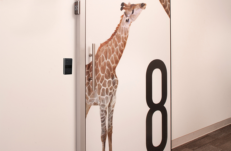 Automatic sliding door in a healthcare facility featuring a sensor and decorated with two giraffe designs.