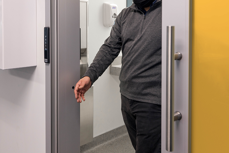 Person exiting a room through an automatic sliding door, activated by a press button.