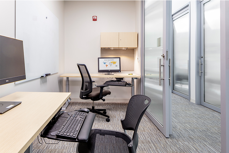 A study room in Santa Rosa Community College with two desks and computers, showcasing a sliding door that opens to a hallway with similar sliding doors. 